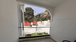 Un balcón con vistas a un área exterior cercada, una silla y piso de baldosas.