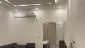 Una sala de estar moderna con un sofá seccional, un televisor de pantalla plana sobre un mueble de madera y un aire acondicionado instalado en el techo.