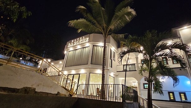 Un hotel con diseño moderno, que destaca una escalera prominente que lleva a la entrada, un frente iluminado y una palmera en primer plano.