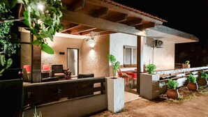 Un patio al aire libre con una zona de estar de hormigón, una pérgola de madera y plantas en macetas.