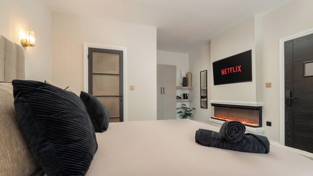 A bedroom with a bed, a TV mounted above a fireplace, and a door labeled "NETFLIX".