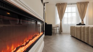 A modern hotel room with a fireplace, a bed, a chair, and a window with curtains.