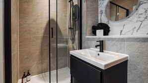 A modern bathroom with a glass-enclosed shower, a white sink, and a marble-tiled wall.