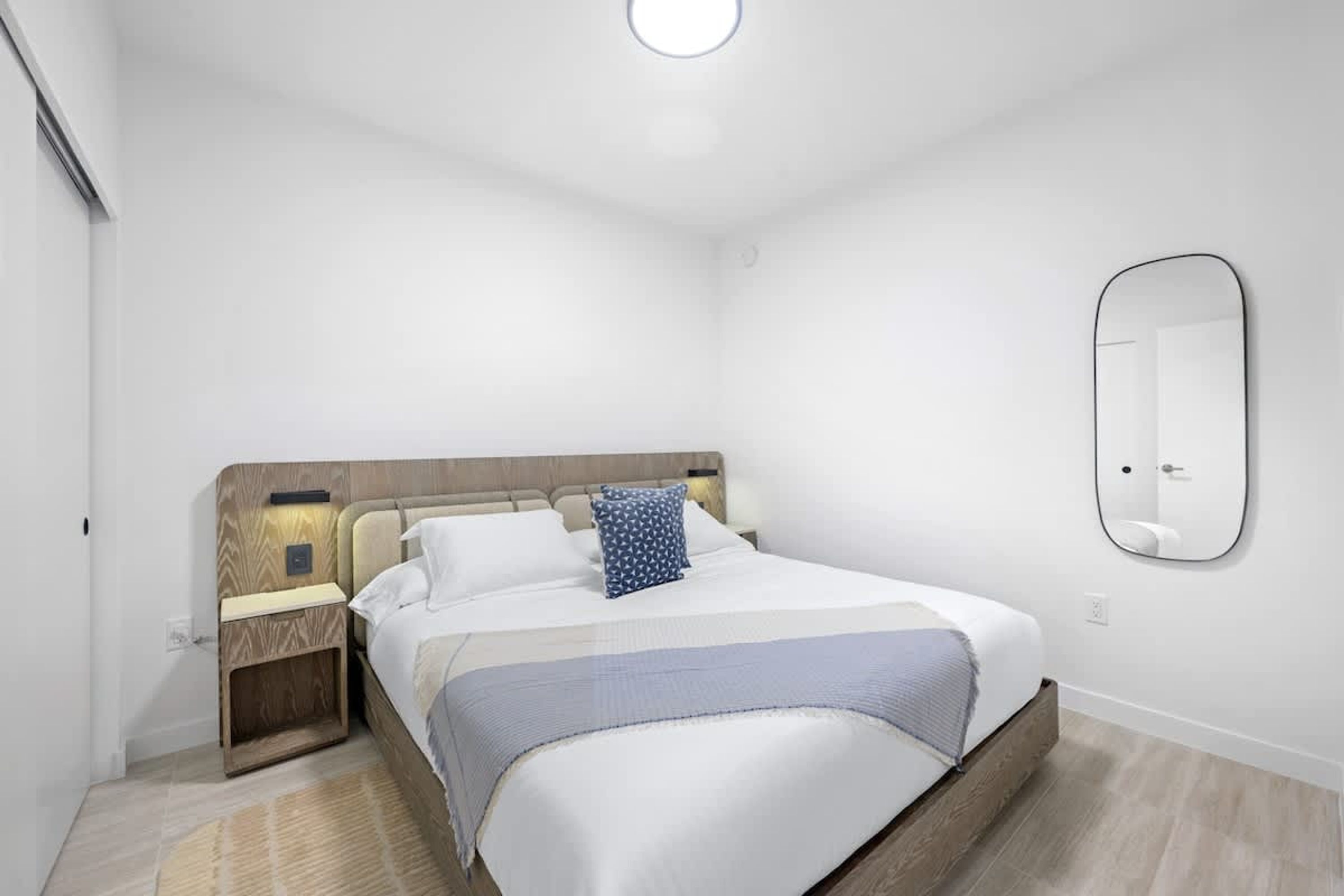 A neatly arranged bedroom with a bed, bedside tables, a mirror, and a light fixture.