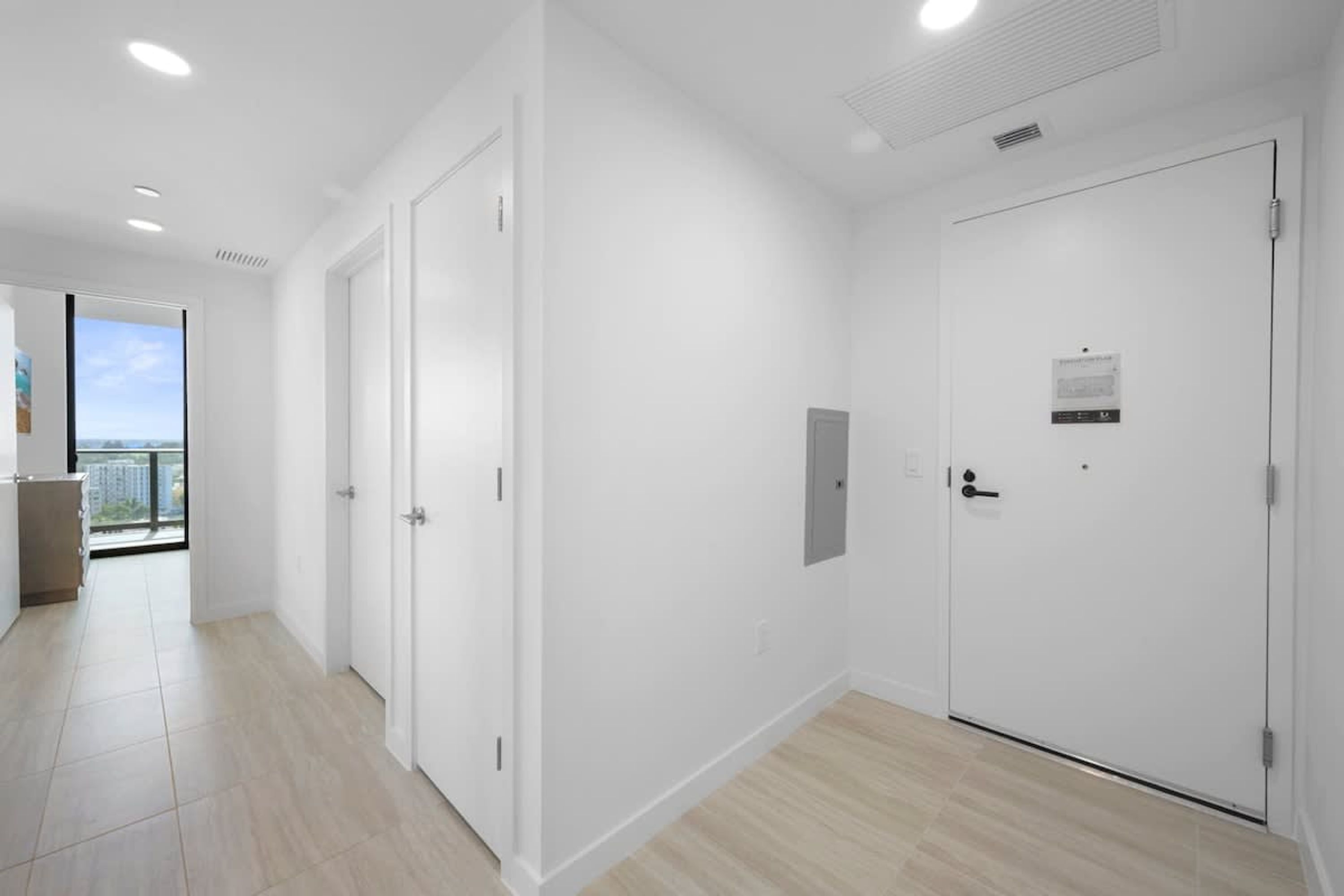 A modern hotel room with white walls, a wooden floor, and two white doors.