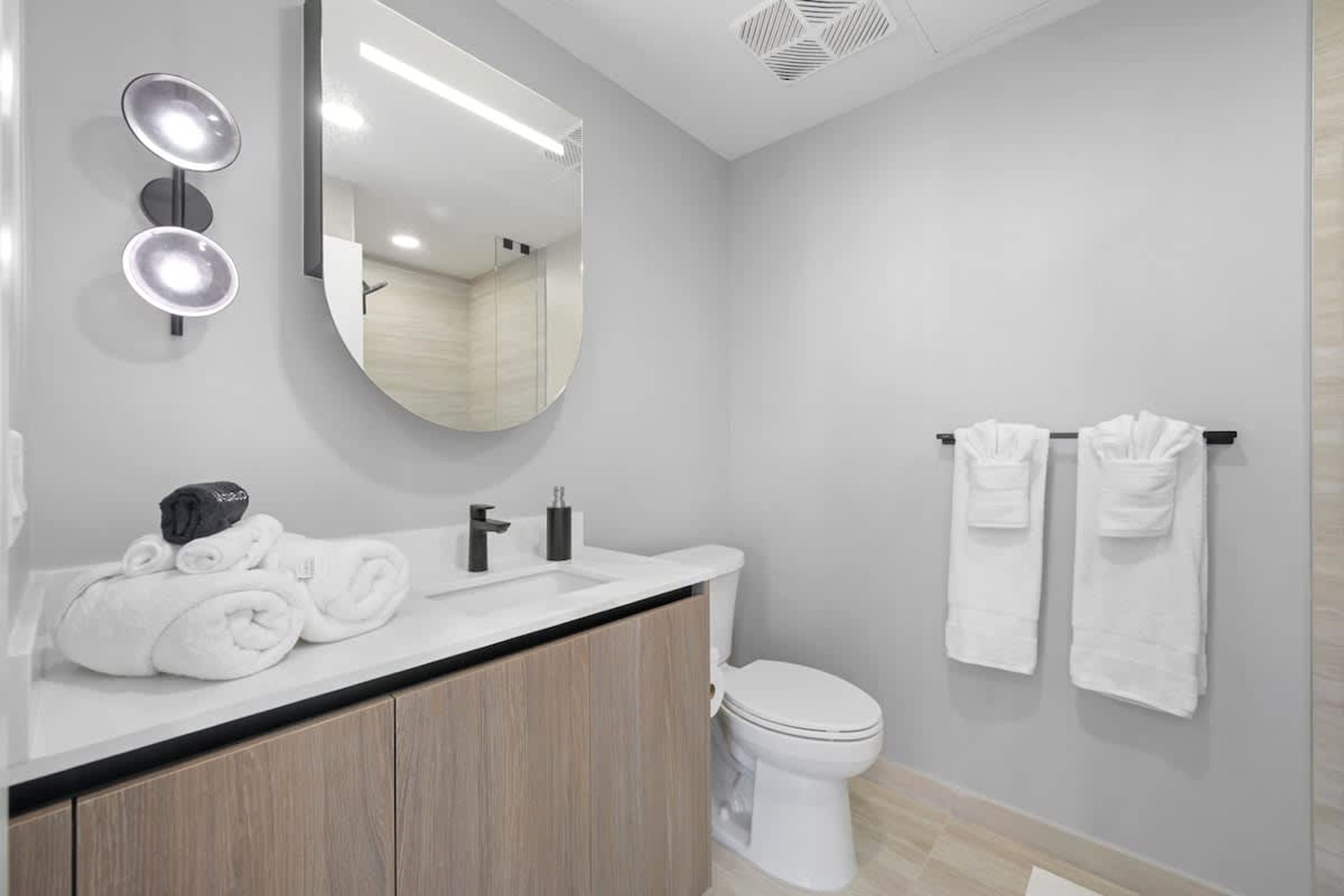 Une salle de bain moderne avec un meuble-lavabo en bois, un miroir rond et des toilettes.