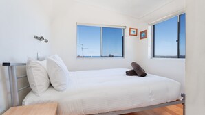 Une chambre à coucher minimaliste, avec un lit, une petite table et deux fenêtres donnant sur le ciel et le paysage.