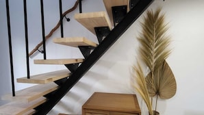 Una escalera con escalones de madera y barandillas de metal negro, un pequeño banco de madera y una cesta tejida con plantas secas.