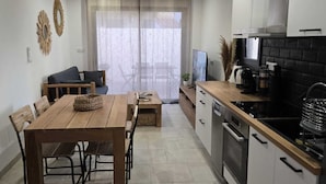 Una cocina moderna con zona de comedor, que incluye una mesa y sillas de madera, un horno empotrado y un amplio ventanal con cortinas translúcidas.