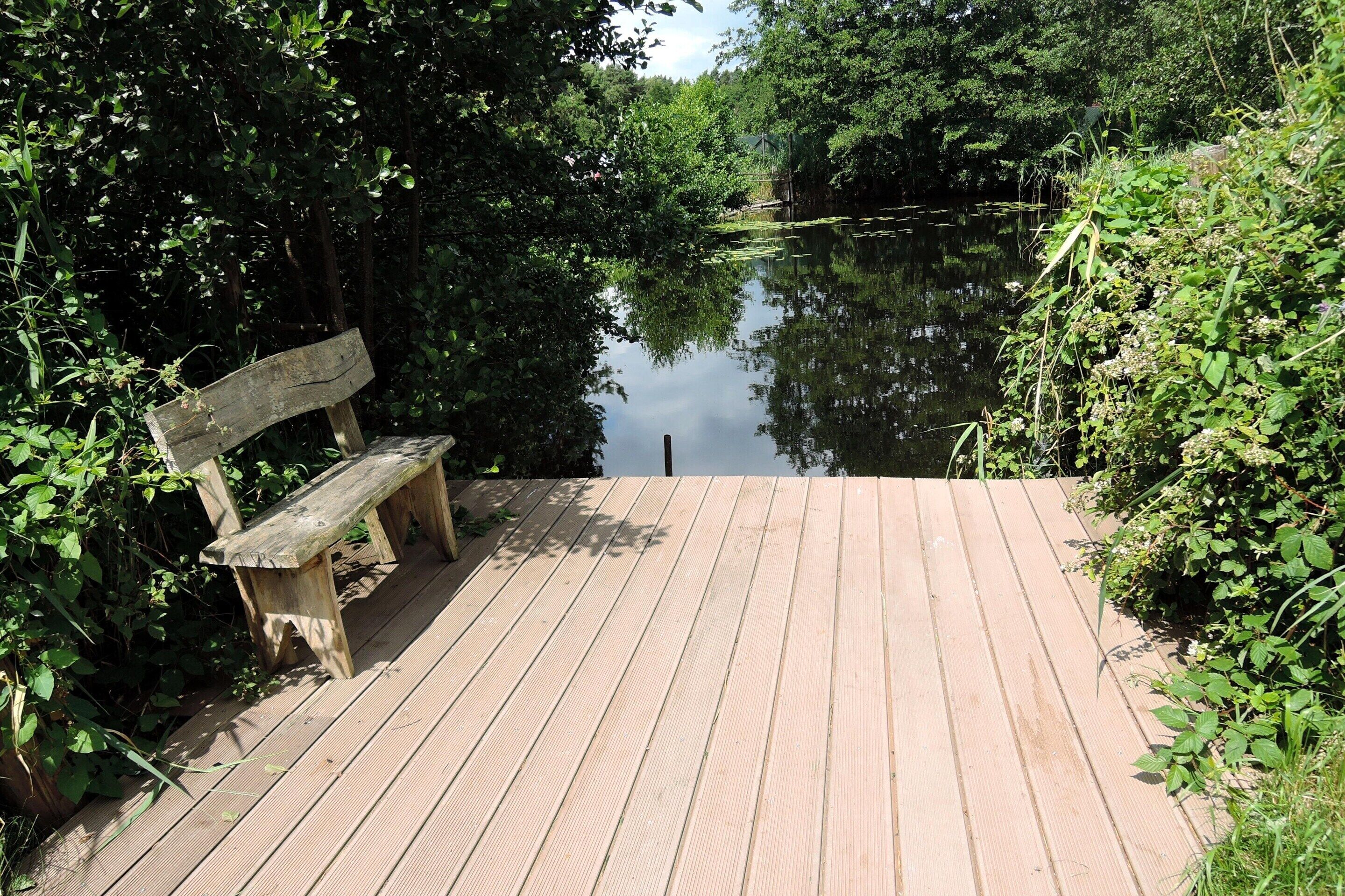 A wooden deck with a bench overlooking a calm body of water, surrounded by dense greenery.