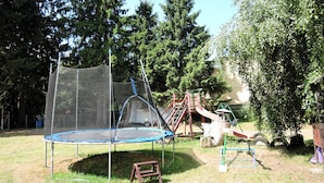 A trampoline with a safety net, a slide, and a swing set in a grassy area with trees in the background. - Kolczewo Lake & Forest Farm Stay (gmina Wolin)