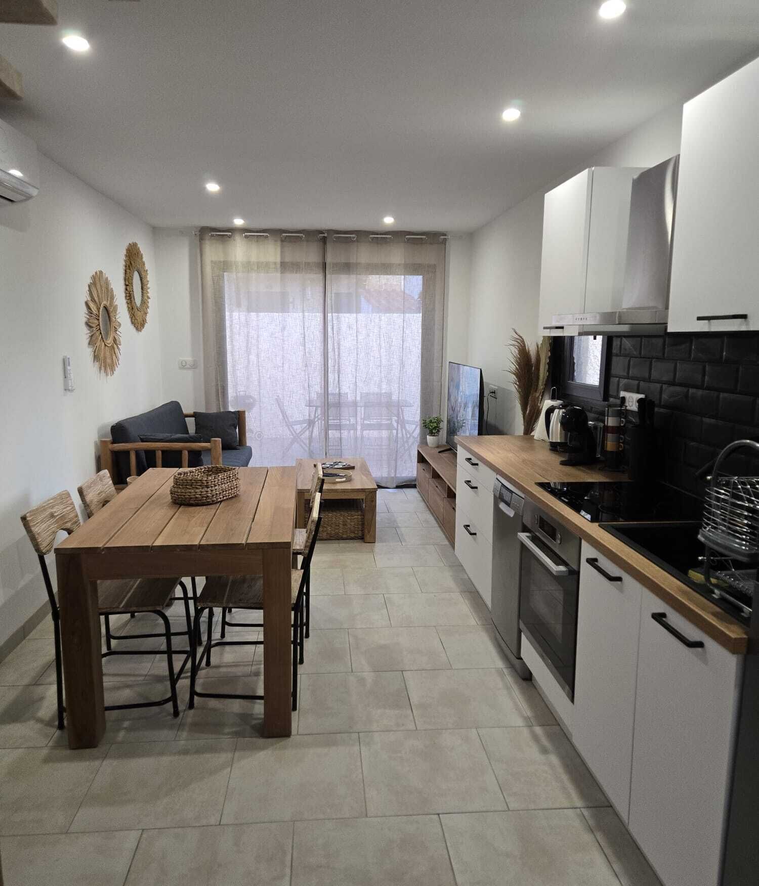 Eine moderne Küche mit Essbereich, ausgestattet mit einem Holztisch und -stühlen, einem eingebauten Backofen und einem großen Fenster mit leichten Vorhängen.