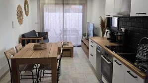 A modern kitchen with a dining area, featuring a wooden table and chairs, a built-in oven, and a large window with sheer curtains.