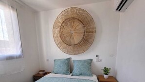 A bedroom with a bed, two pillows, a bedside table with a plant, and a wall-mounted decorative item.