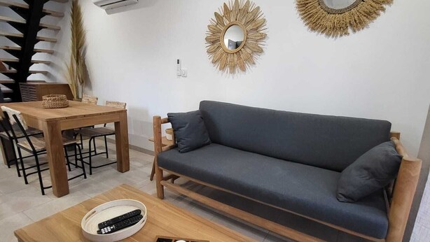 A modern living room with a sofa, a wooden coffee table with a board game, a dining table with chairs, and two decorative mirrors on the wall.