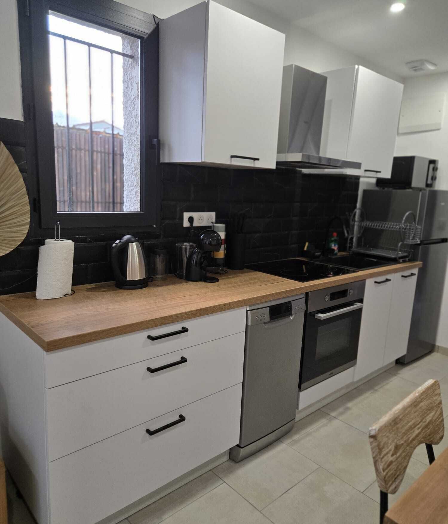 A modern kitchen with white cabinets, a wooden countertop, stainless steel appliances, and a window with a view of a fence.