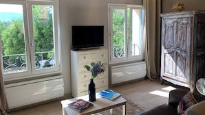 A living room with a TV, a wooden cabinet, a sofa, and a window with a view of greenery.