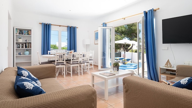 Una sala de estar con comedor, ventilador de techo, televisor y vistas al exterior.