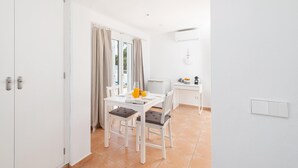 Una habitación pequeña con una mesa de comedor, sillas, una kitchenette y una puerta que conduce a otra habitación.