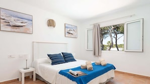 Un dormitorio con cama, mesita de noche, lámpara, ventana con cortinas y dos cuadros en la pared.