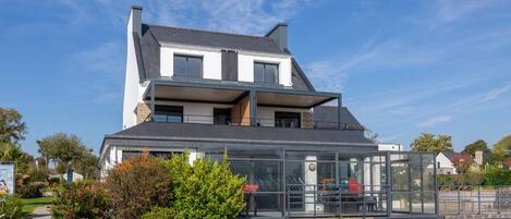 A two-story house with a glass entrance, a visible balcony, and a garden area.