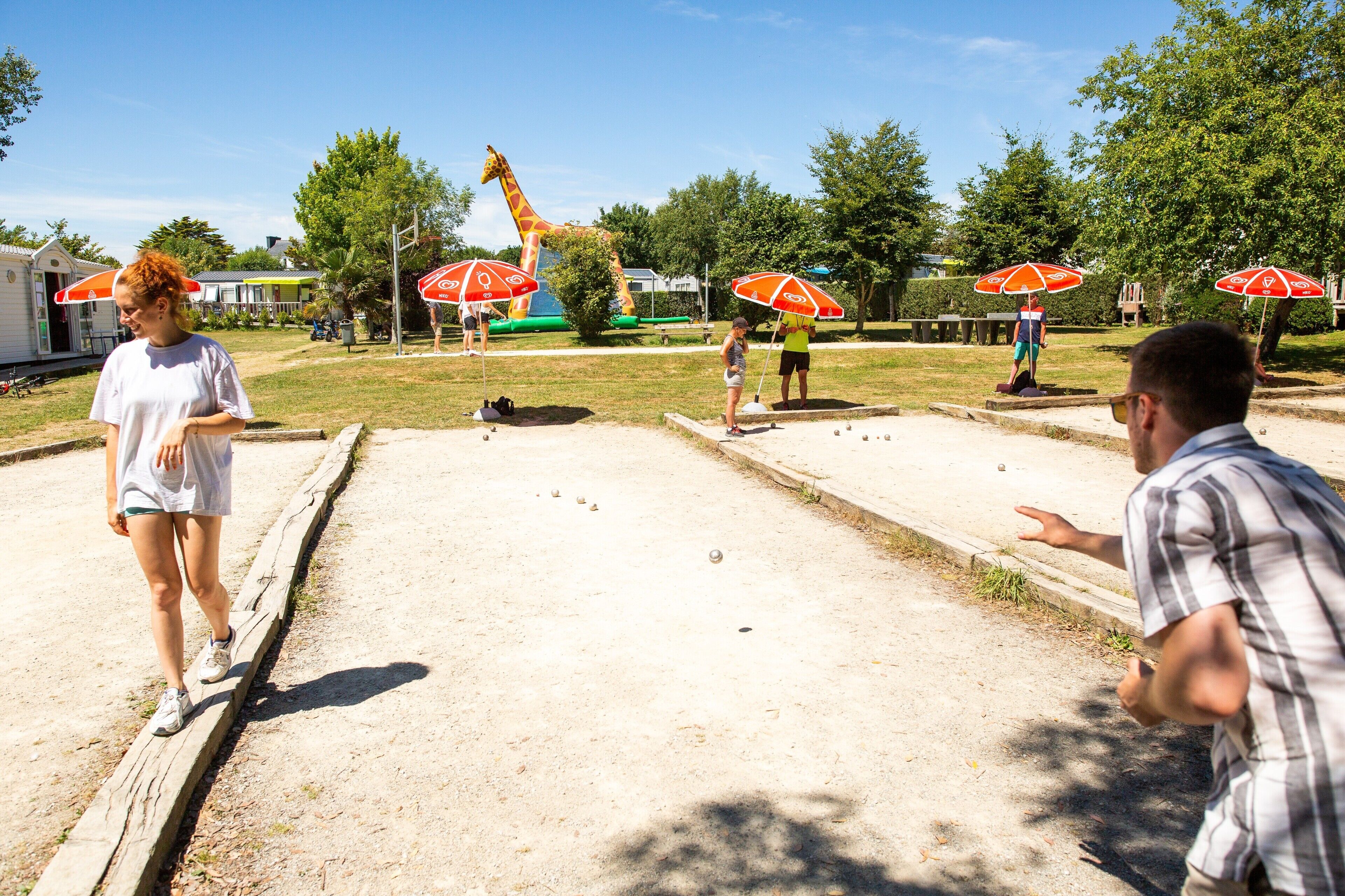 A billiards table with people playing, surrounded by trees and a giraffe sculpture.
