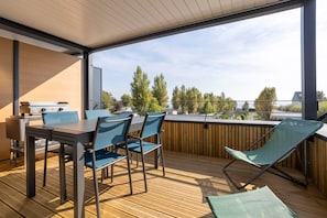 Um terraço com mesa, cadeiras, churrasqueira e vista para árvores e edifícios.
