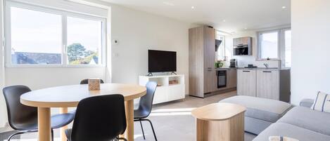 A modern living room with a round dining table, black chairs, a grey sofa, and a small wooden side table.