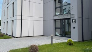 Ein modernes Gebäude mit Flachdach, großen Fenstern und einer gepflasterten Eingangsbereits mit kleinem Rasen und Strauch.