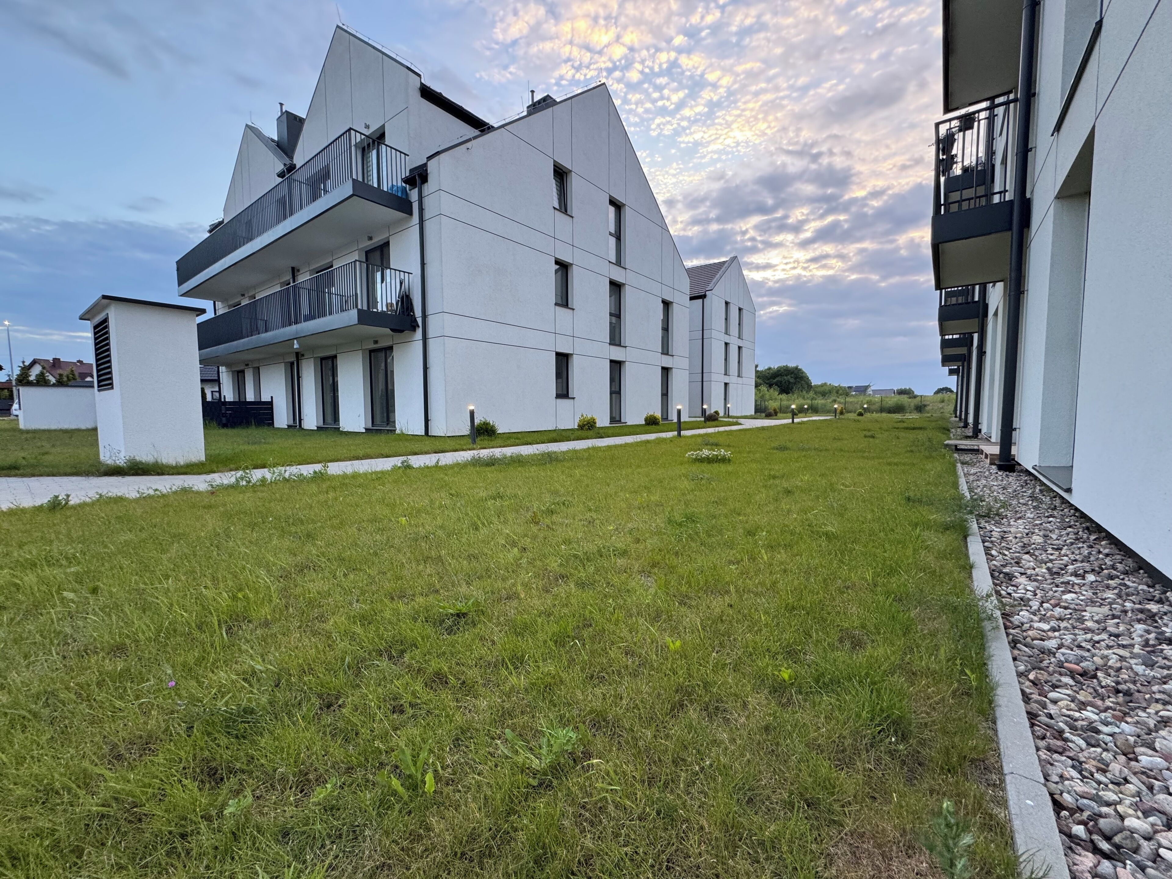 A modern building with a flat roof, multiple balconies, and a well-maintained lawn.