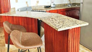 Eine Küche mit Holzausstattung, einer Granit Arbeitsplatte, einer integrierten Kochinsel mit Barhocker, einem Mixer und einem Kühlschrank.