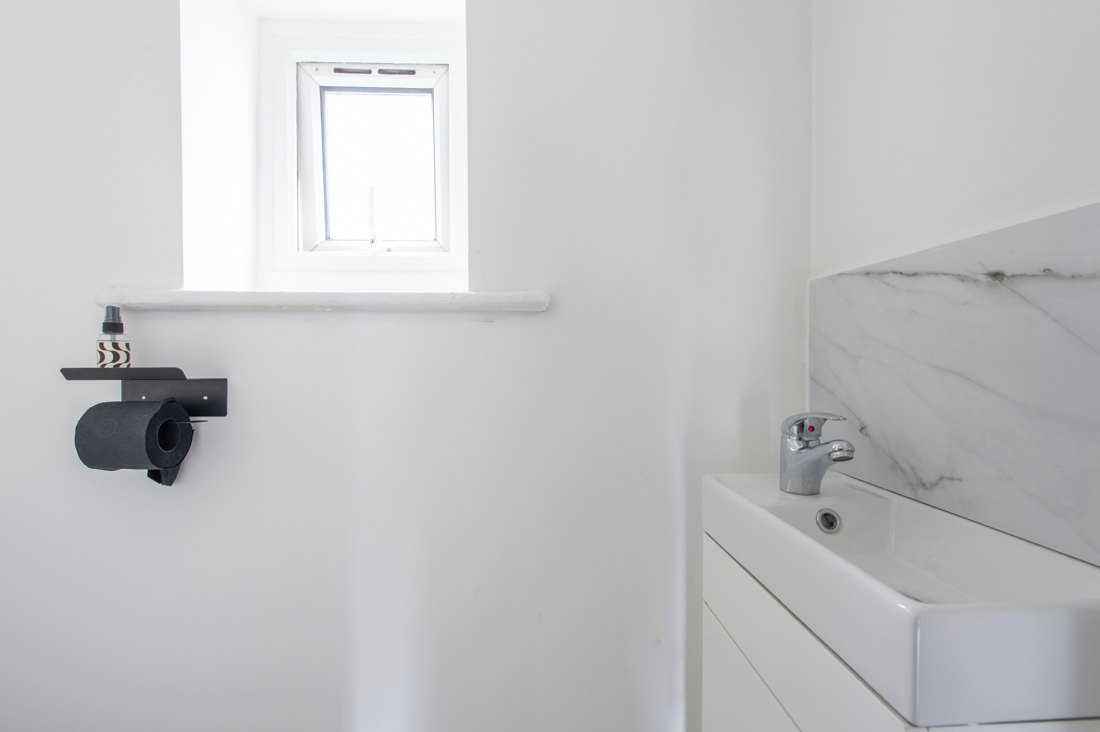 A bathroom with a white sink, a marble countertop, and a window above the sink.