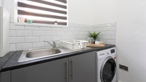 A kitchen with a sink, a washing machine, and a window with blinds. - Apt - Stay 6 - Paid Parking - Petsok - Stratford (London)