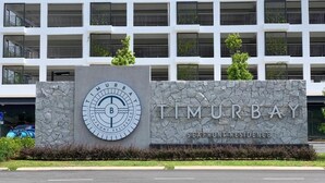 Um edifício com uma placa que diz "Timurbay Seafront Residence" e um logotipo circular com uma bússola e a letra 'B'.