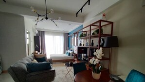 Uma sala de estar moderna com um sofá, uma mesa de jantar com cadeiras, uma estante e um lustre.