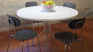 A round dining table with a white surface and four black chairs. A white bowl with grapes and other fruits is placed on the table. A white pendant light hangs above the table. The wall behind has a textured, abstract mural. - Bright apartment in the historic center Santo Spirito fully restored (Firenze)