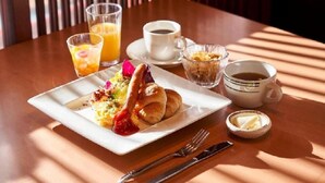 Een ontbijtsetting met croissants, sinaasappelsap, koffie en een klein schaaltje boter op een houten tafel.