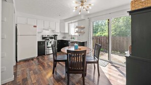 A kitchen with white cabinets, a wooden dining table, and a large window. - The StayBerry - Stay for 6 (Columbus)