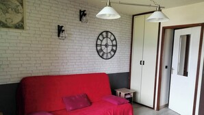 A room with a red sofa, a small table, a clock, and a wardrobe.