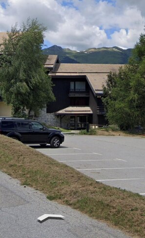 A building with a parking lot, a black SUV parked in front, and mountains in the background. - Ski-to-door gondola access studio la plagne montalbert (Aime-la-Plagne)