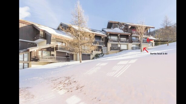 A modern ski resort building with multiple balconies and a ski slope in the foreground.