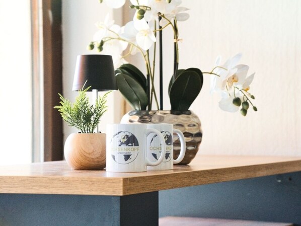 A wooden table with a potted plant, a lamp, and three mugs with text. - Ochsenkopf apartment (Bischofsgrün)