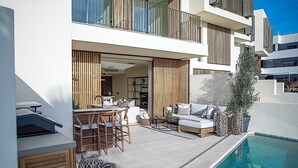 A modern outdoor living area with a pool, wooden furniture, and a view of the building's interior. - Exclusive Duplex Apartment in Talamanca (Santa Eulalia del Río)