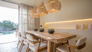 A modern dining area with a wooden table, white chairs, and three woven pendant lights. - Exclusive Duplex Apartment in Talamanca (Santa Eulalia del Río)