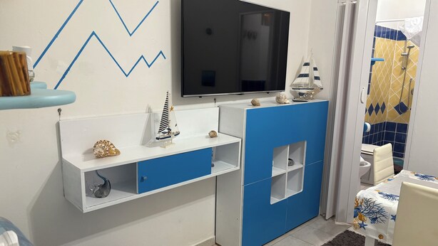 Ein modernes Badezimmer mit weiß-blauer Farbgestaltung, einem angebrachten Fernseher und einem kleinen Segelbootmodell auf der Ablagefläche.