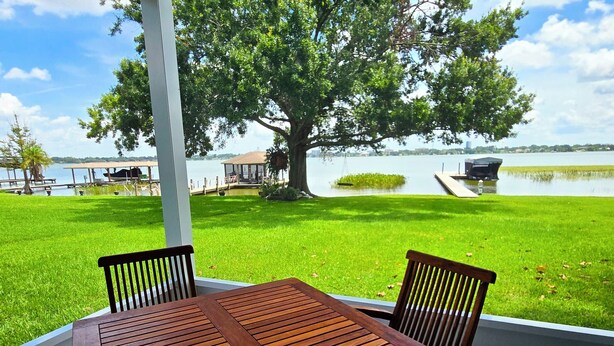 A wooden table and chairs on a deck with a view of a lake and dock area.