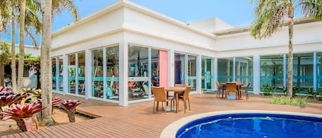 A modern building with glass walls, a pool, and outdoor seating.
