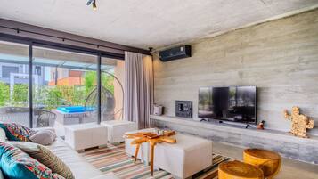 Uma sala de estar moderna com um sofá, um banquinho e banquetas de madeira. Uma televisão de tela plana está fixada na parede, e há uma lareira abaixo.