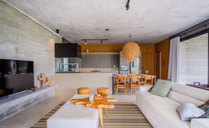 A modern living room with a sofa, coffee table, and TV. There is a kitchen area with a dining table and chairs. - Modern House With Pool Next to Surfland Roi00 (Garopaba)