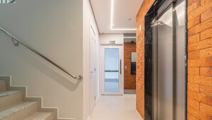 Un couloir moderne avec un escalier, une porte vitrée et un ascenseur.